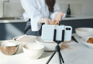 Close up view of back of device setup in tripod on counter in kitchen, capturing woman’s hands cooking using carrots and bowls