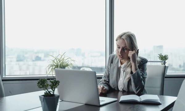 Businesswoman speaking and engaged in a serious video call seated at head of table in conference room near large windows