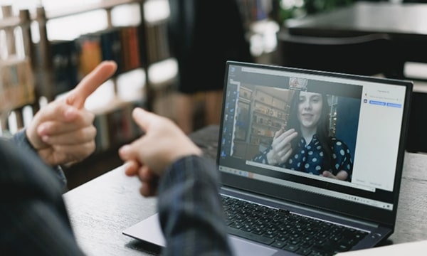 Side view of gesticulating hands in front of an opened laptop using video chat to communicate with a woman onscreen also using hands to express an idea