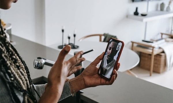 Woman in kitchen video chatting with man on smartphone in her left hand, and using right hand to communicate and express emotion